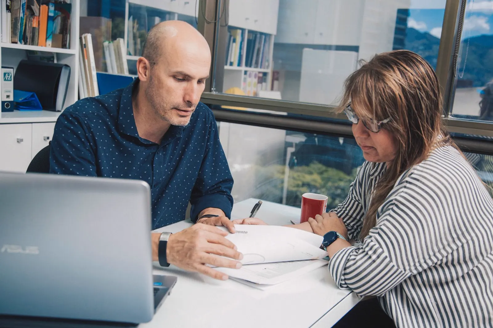 Two people review work documents next to a laptop